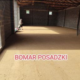 Bomar - Wnętrze hali z wylewką jastrychową w odcieniach beżu, widoczny pracownik z narzędziami w tle, ściany z szarych bloczków betonowych, logo BOMAR POSADZKI na pierwszym planie.