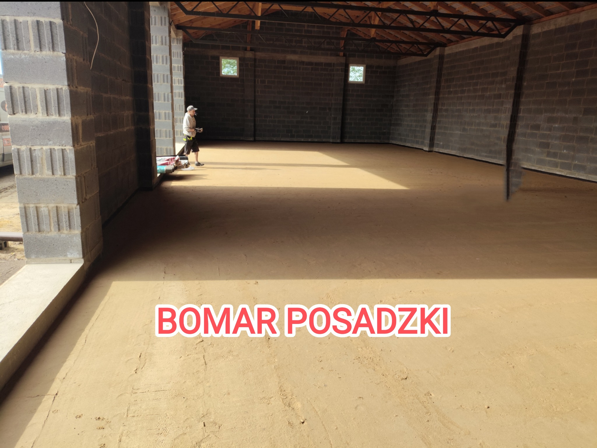Wnętrze hali z wylewką jastrychową w odcieniach beżu, widoczny pracownik z narzędziami w tle, ściany z szarych bloczków betonowych, logo BOMAR POSADZKI na pierwszym planie.
