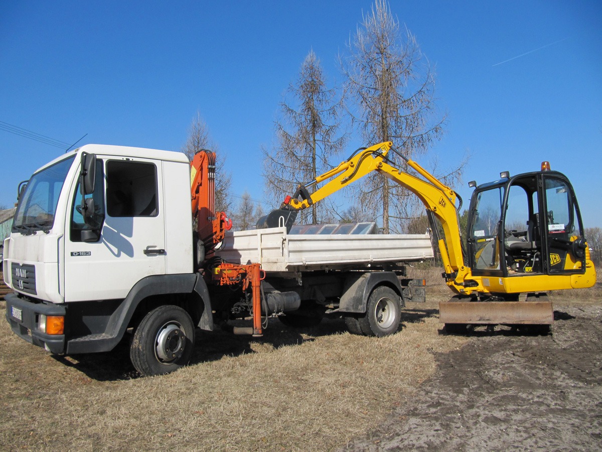 Biała ciężarówka MAN z pomarańczowym dźwigiem HDS przewozi żółtą minikoparkę JCB na przyczepie, widok z boku na tle błękitnego nieba i suchych traw.