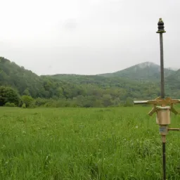 Urządzenie do pobierania próbek gruntu na łące, w tle zalesione wzgórza i pochmurne niebo.
