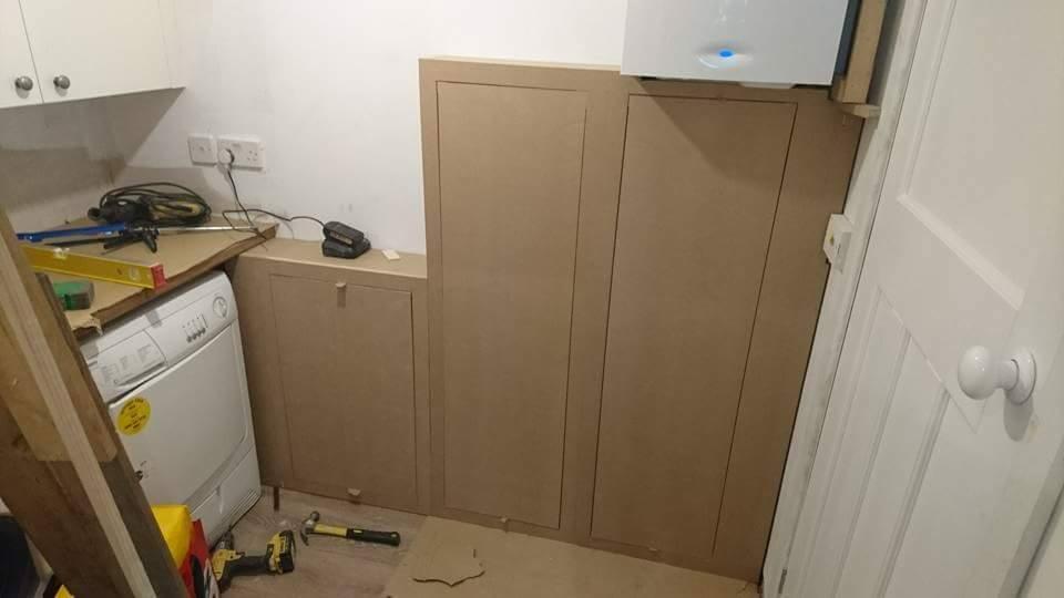 Montaż zabudowy z surowej płyty MDF w małej łazience z pralką, widoczne narzędzia i poziomica.