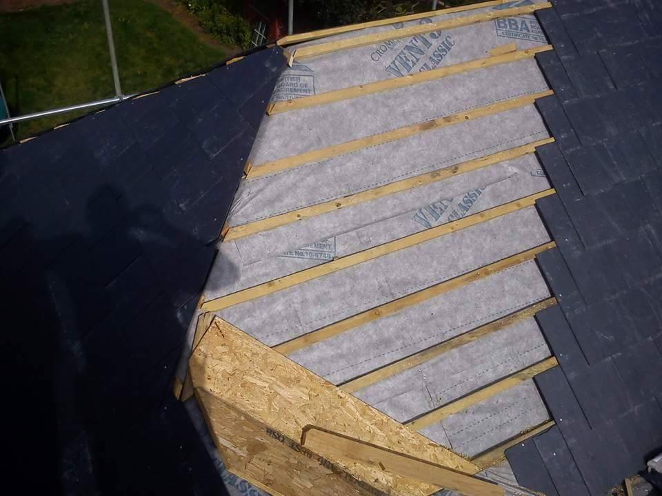 Fragment dachu w trakcie montażu: widoczne drewniane łaty, membrana dachowa z nadrukiem 'VENT CLASSIC' oraz częściowo ułożone ciemne płytki dachowe. U dołu widoczny fragment konstrukcji z płyty OSB.