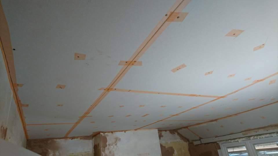 Przygotowanie sufitu do montażu płyt kartonowo-gipsowych: widoczne listwy mocujące i taśmy maskujące na powierzchni sufitu, ściany w stanie surowym, okno w tle.