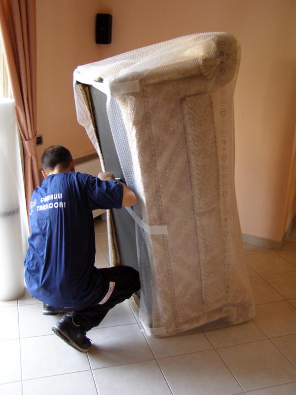 Pracownik w niebieskiej koszulce zabezpiecza mebel folią bąbelkową i taśmą podczas przygotowań do transportu.
