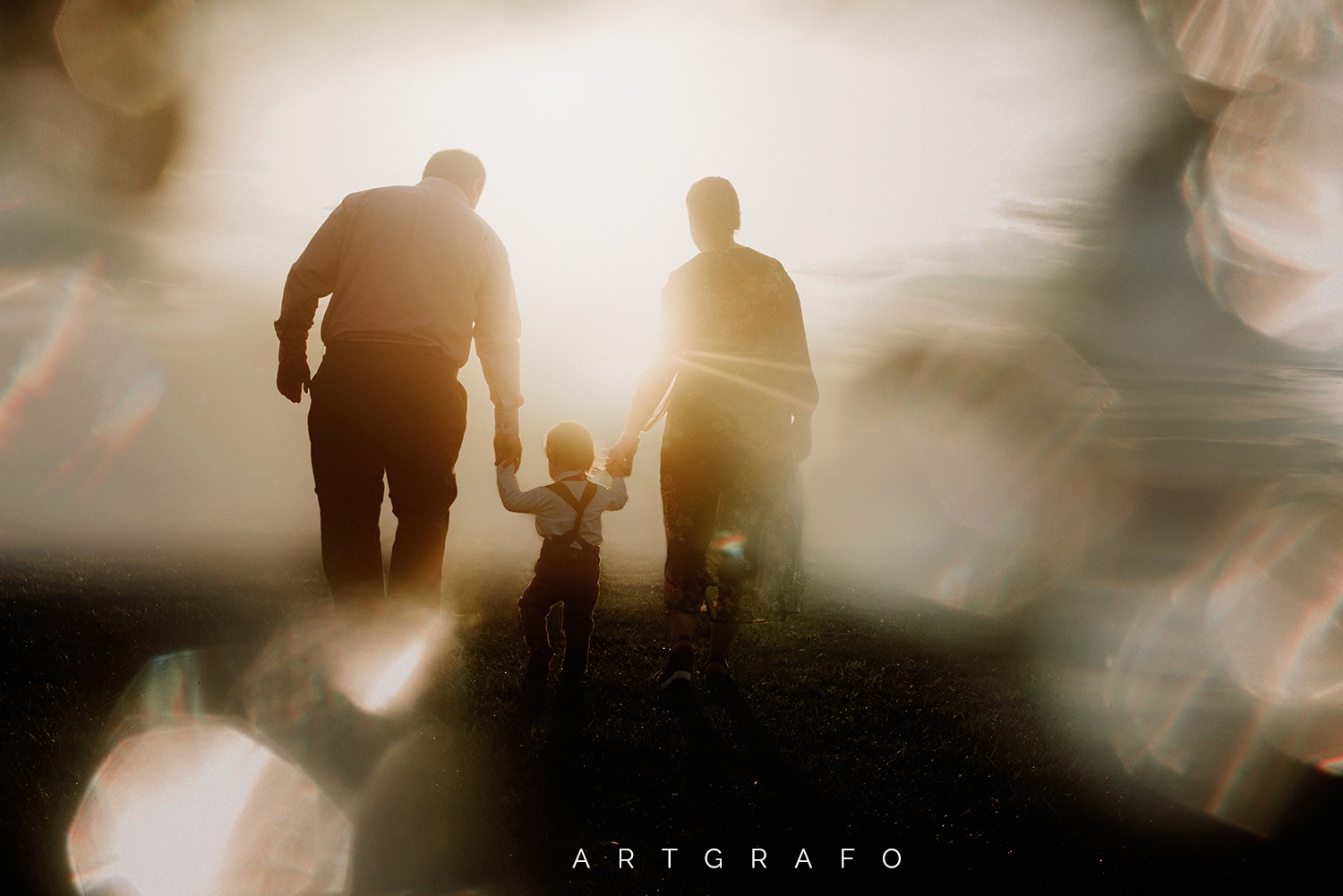 Sylwetki rodziny (ojciec, matka i małe dziecko) idącej pod słońce, z efektem bokeh w tle i pierwszym planie.