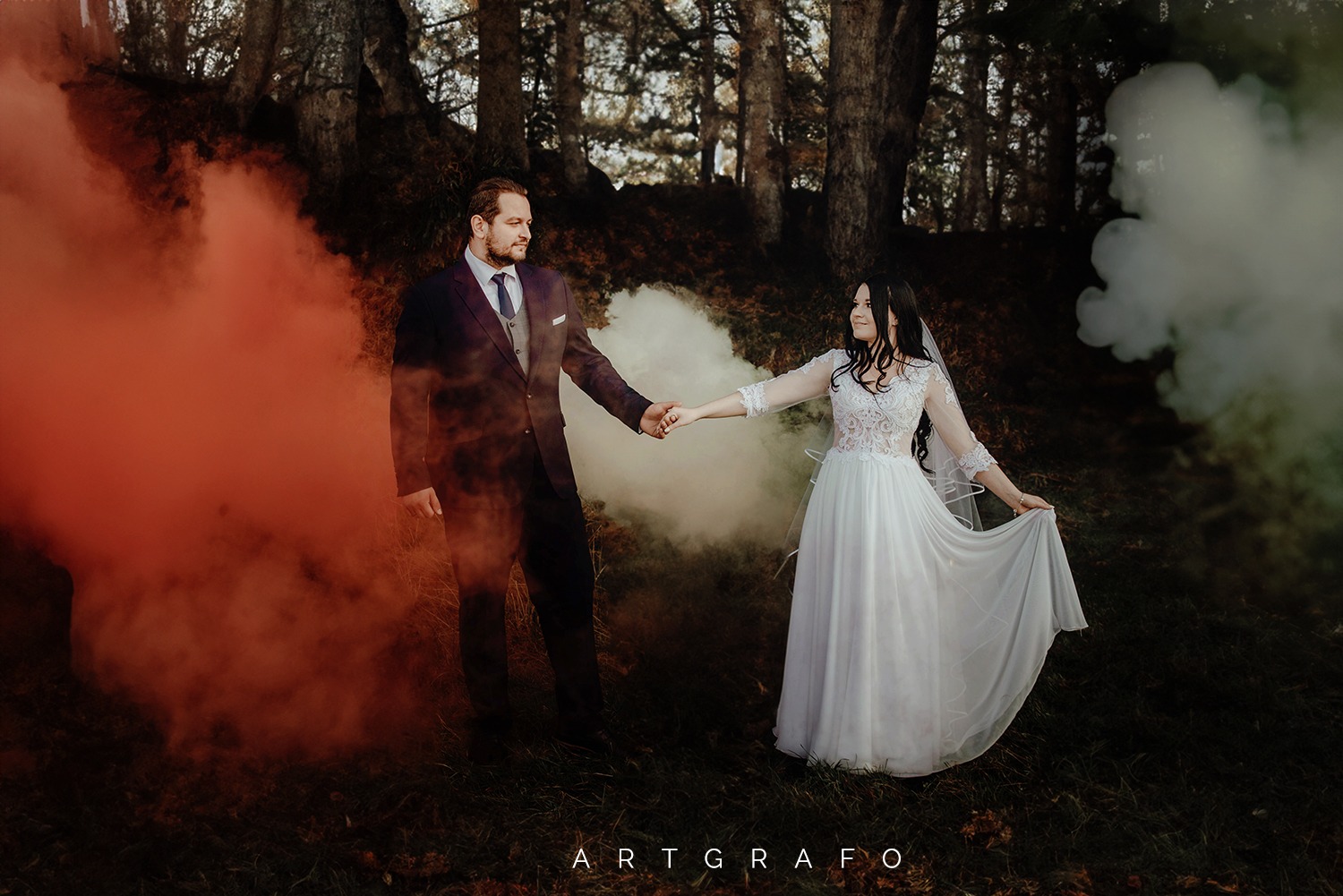 Para młoda trzymająca się za ręce w lesie, otoczona kolorowymi smugami dymu.