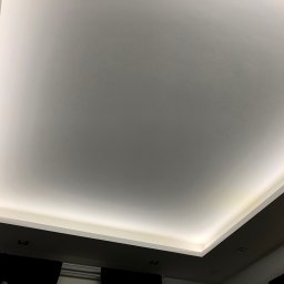 S-BAU USŁUGI OGÓLNOBUDOWLANE STANKIEWICZ - Nowoczesny sufit podwieszany z oświetleniem LED, widok z dołu, czarne zasłony w tle.