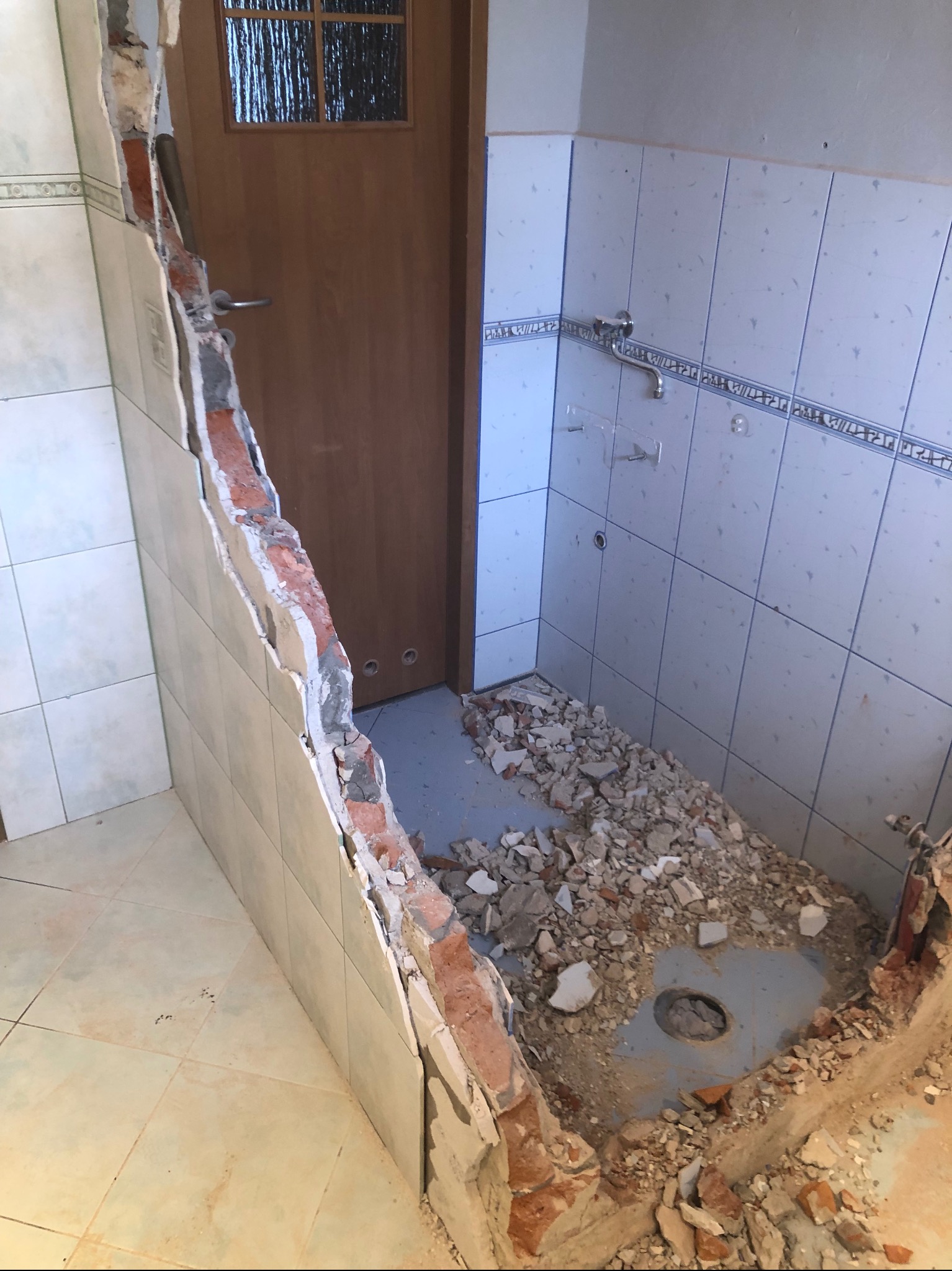 Demontaż płytek w łazience, odsłonięta cegła i gruz na podłodze, widoczny odpływ pod prysznicem, przygotowanie do remontu.