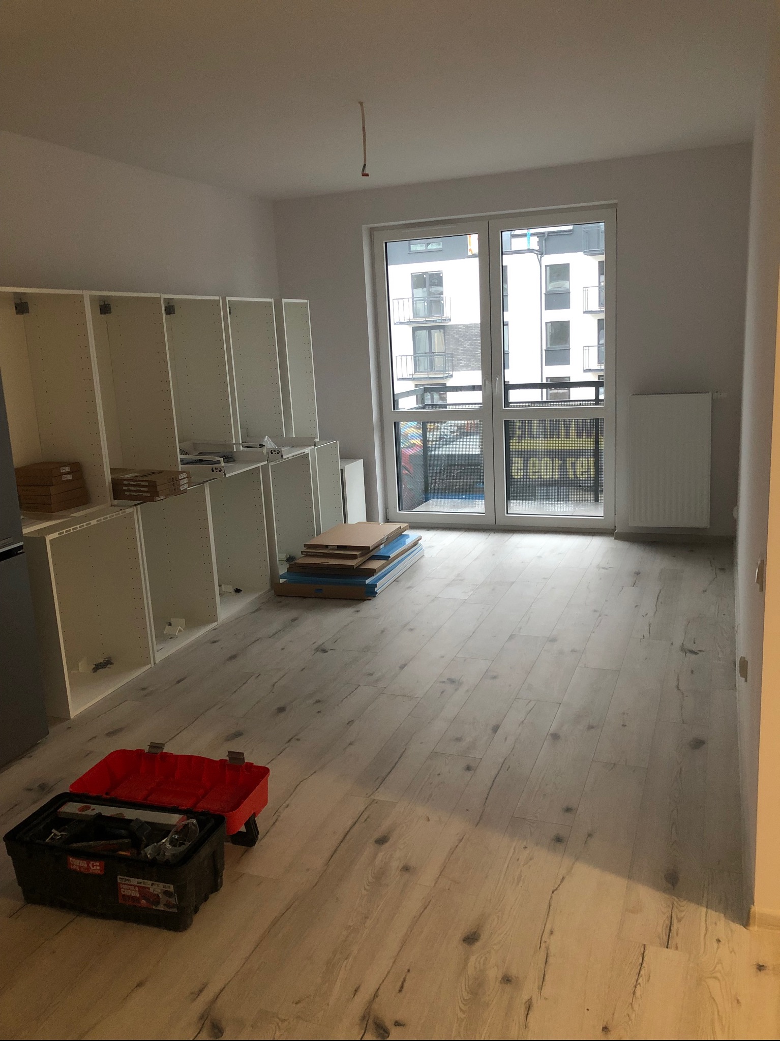 Montaż szafek kuchennych w nowym mieszkaniu w Szczecinie, widoczne rozpakowane elementy i skrzynka z narzędziami na podłodze.