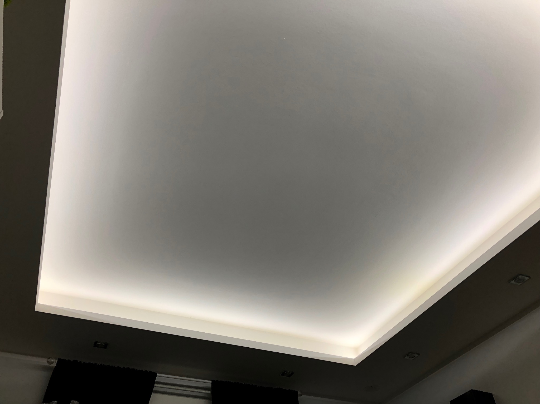 Nowoczesny sufit podwieszany z oświetleniem LED, widok z dołu, czarne zasłony w tle.