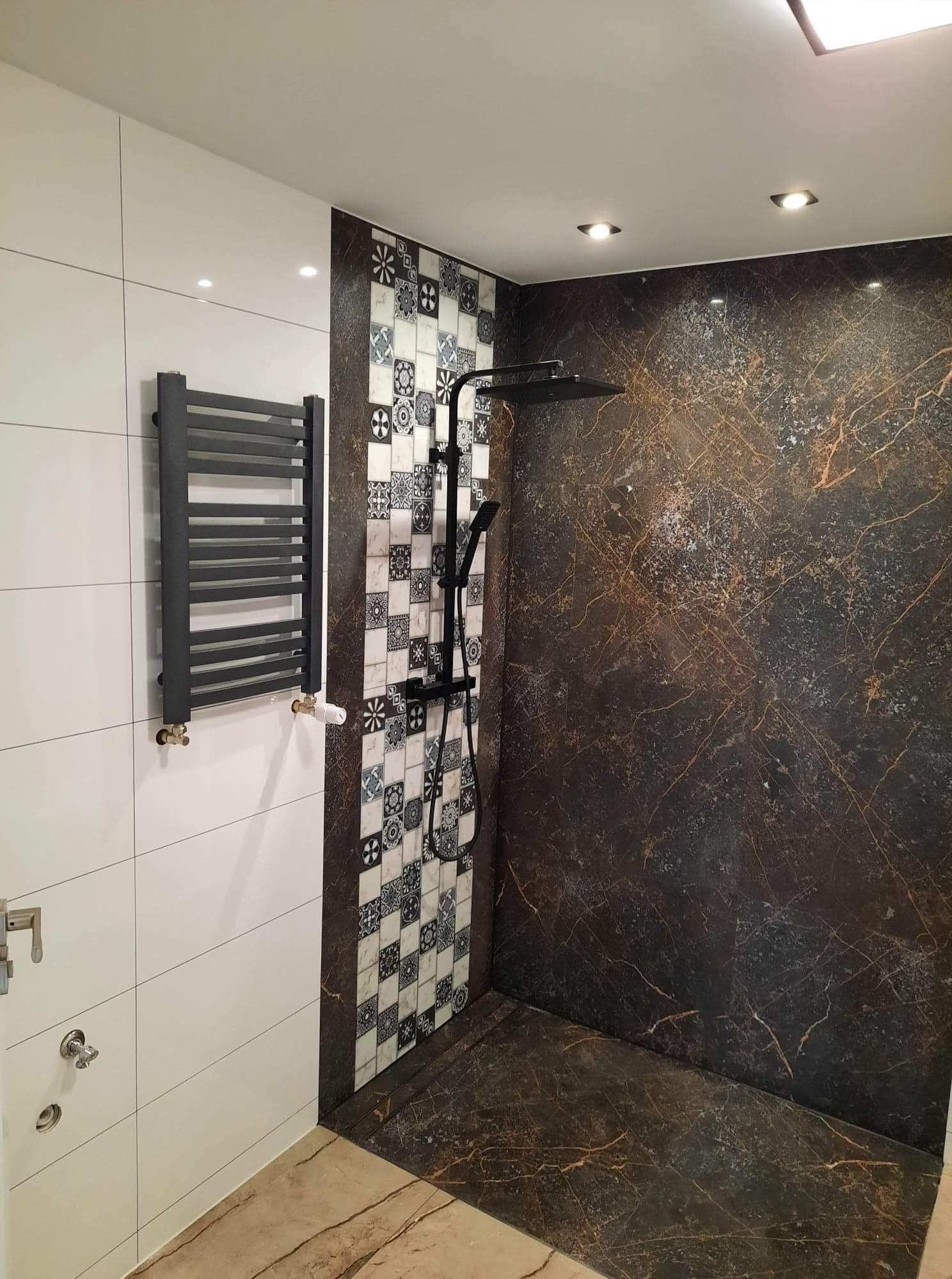 Nowoczesna łazienka z czarną armaturą, grzejnikiem drabinkowym na białych płytkach i ścianą prysznicową z płytek imitujących marmur.