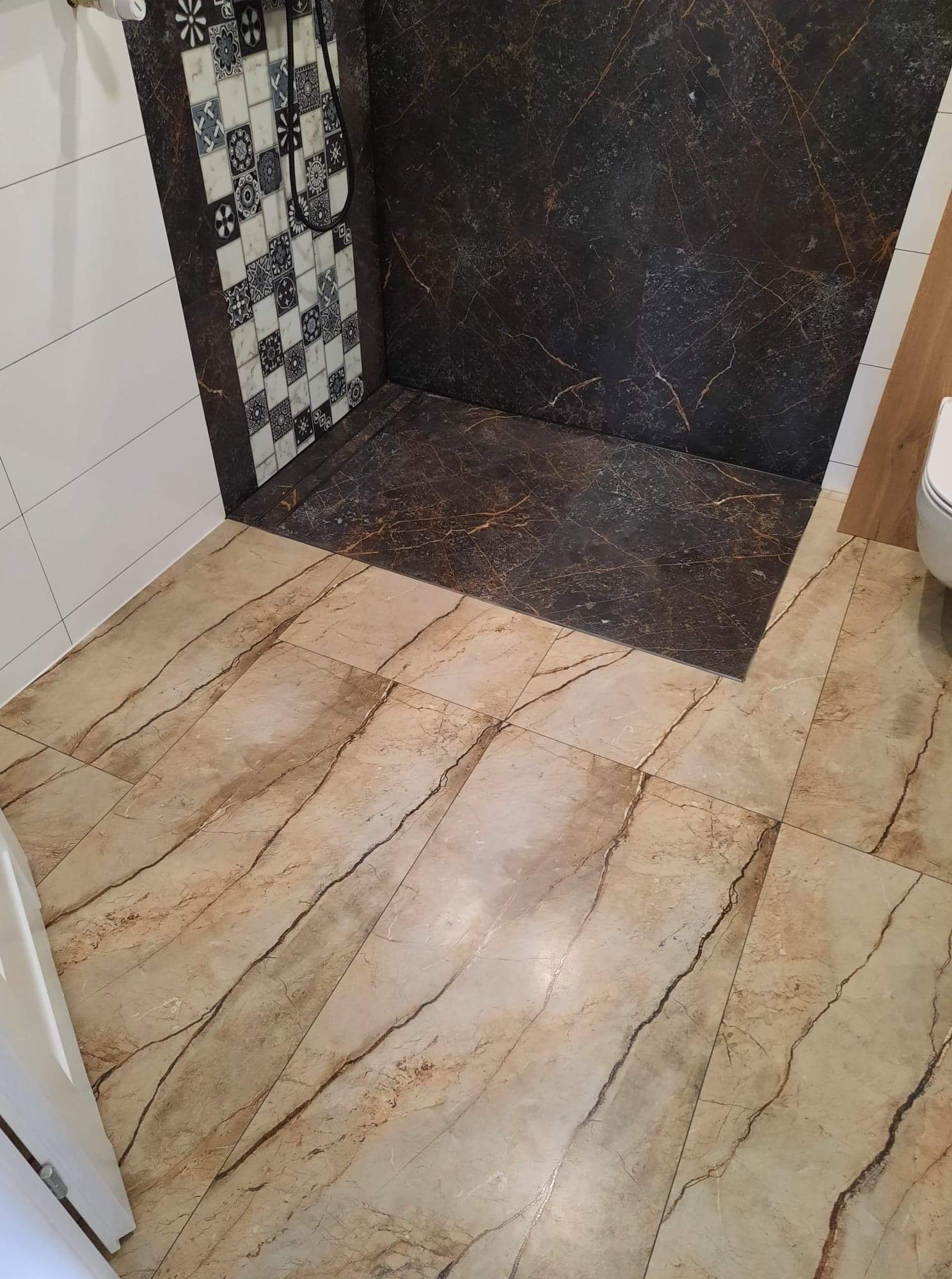 Ukończona łazienka z brązowymi marmurkowymi płytkami pod prysznicem i mozaikową ścianą, oraz beżowymi płytkami podłogowymi z ciemniejszymi żyłami.