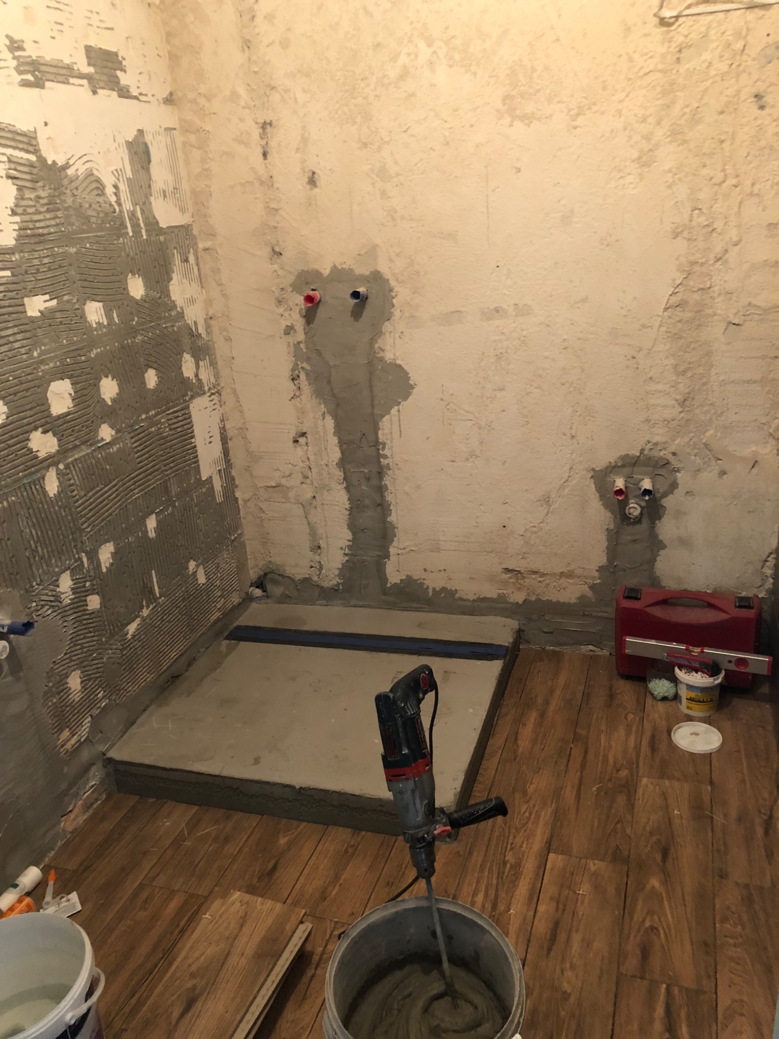 Przygotowanie wylewki w łazience: widok na mieszadło do zaprawy w wiadrze, częściowo położone płytki na ścianach, przygotowany brodzik, oraz narzędzia w czerwonej skrzynce.