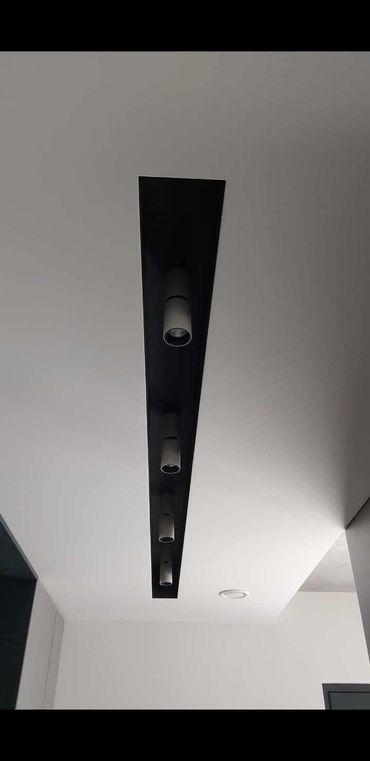 Minimalistyczny sufit z czarną wnęką i rzędem cylindrycznych, białych reflektorów punktowych, oświetlających wnętrze. Nowoczesny design.