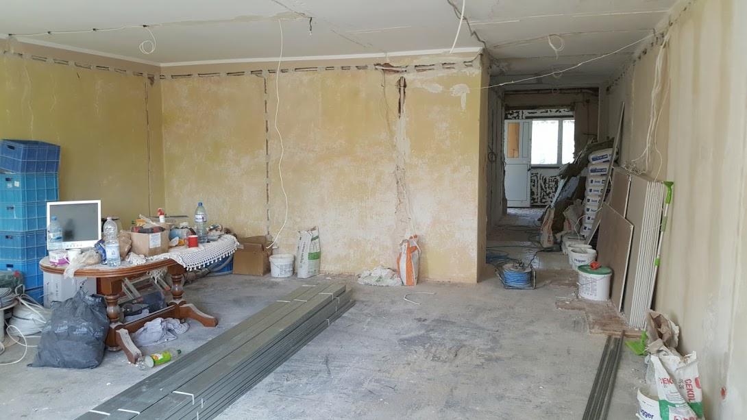Pokój w trakcie remontu: ściany przygotowane do szpachlowania, widoczne bruzdy pod instalacje, na podłodze materiały budowlane, w tle widok na kolejne pomieszczenie.