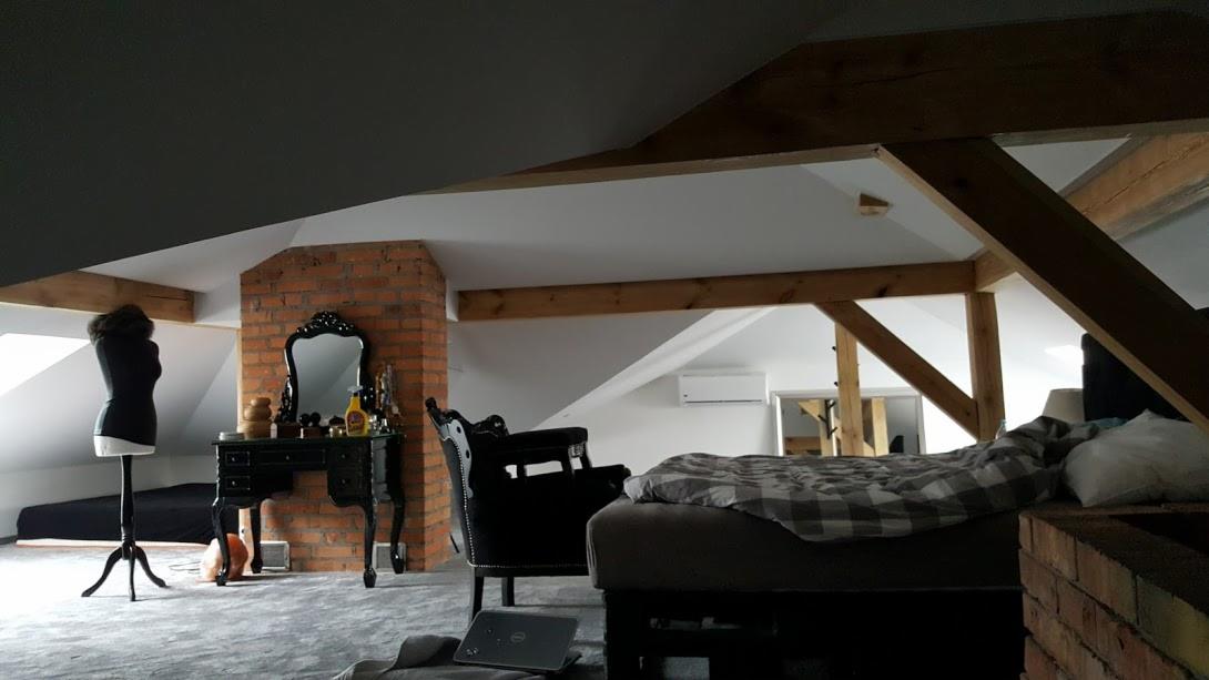 Adaptacja poddasza: sypialnia z widocznymi drewnianymi belkami stropowymi, ceglanym kominem, toaletką z lustrem w stylu retro i manekinem krawieckim.