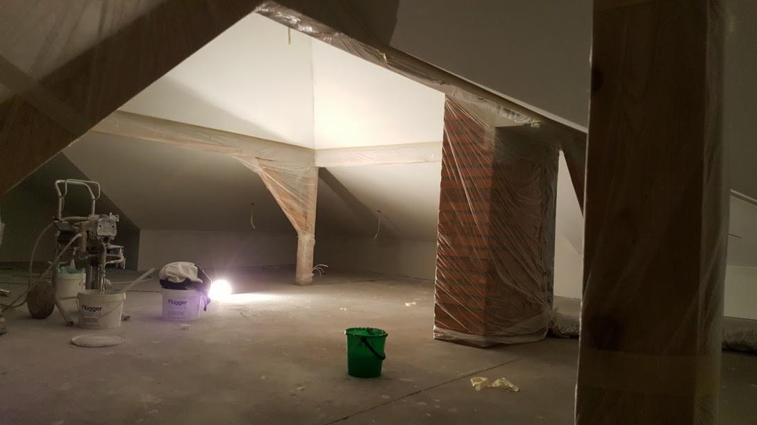 Poddasze w trakcie prac malarskich, zabezpieczone elementy konstrukcyjne, widoczny agregat malarski i puszki z farbą marki Flugger.