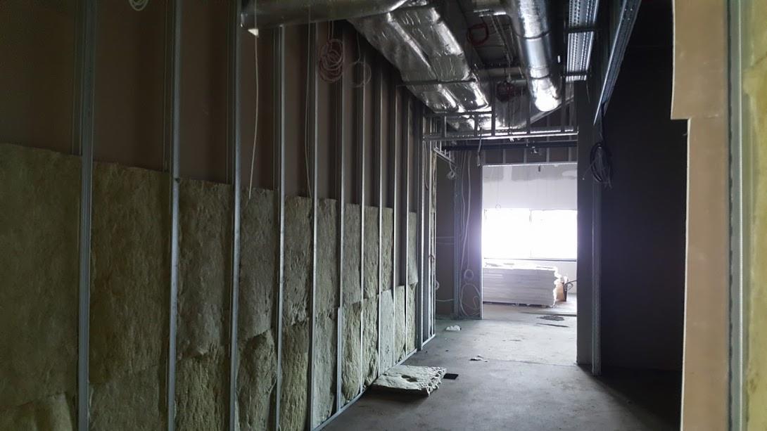 Wnętrze w trakcie budowy: metalowy szkielet ściany z wypełnieniem z wełny mineralnej, widoczne instalacje pod sufitem i przygotowane płyty gipsowo-kartonowe w głębi pomieszczenia.