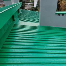 TeamPol - Świeżo pomalowany na zielono blaszany dach z kominem i anteną satelitarną, widoczne krople wody po deszczu.