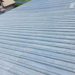 TeamPol - Widok z góry na nową, srebrną blachodachówkę trapezową na budynku, z widocznymi elementami mocującymi i sąsiednimi budynkami w tle.