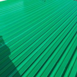 TeamPol - Świeżo pomalowany, jaskrawo zielony, blaszany dach z widocznym cieniem osoby fotografującej, z fragmentem białej ściany w tle.