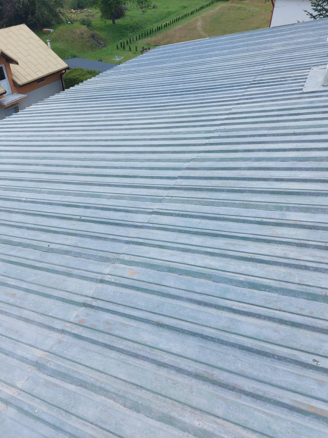 Widok z góry na nową, srebrną blachodachówkę trapezową na budynku, z widocznymi elementami mocującymi i sąsiednimi budynkami w tle.