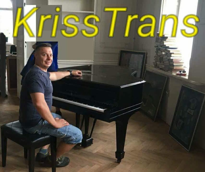 Mężczyzna siedzi na stołku obok czarnego pianina, w tle sterta książek i obrazy, na zdjęciu widoczny napis 'Kriss Trans'.