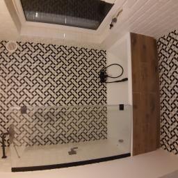 Krzysztof Wojniak - Nowoczesna kabina prysznicowa z czarną armaturą i geometrycznym wzorem płytek na ścianach, oświetlona światłem z okna dachowego.