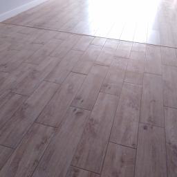 Krzysztof Wojniak - Ułożona podłoga z paneli imitujących drewno, widoczna biała listwa przypodłogowa i fragment podłogi bez paneli, z wyraźnym przejściem między powierzchniami.