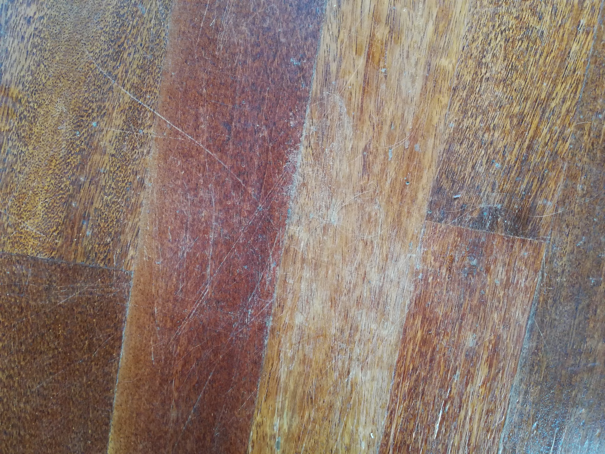 Drewniana podłoga z widocznymi śladami użytkowania, rysami i przetarciami na lakierze.