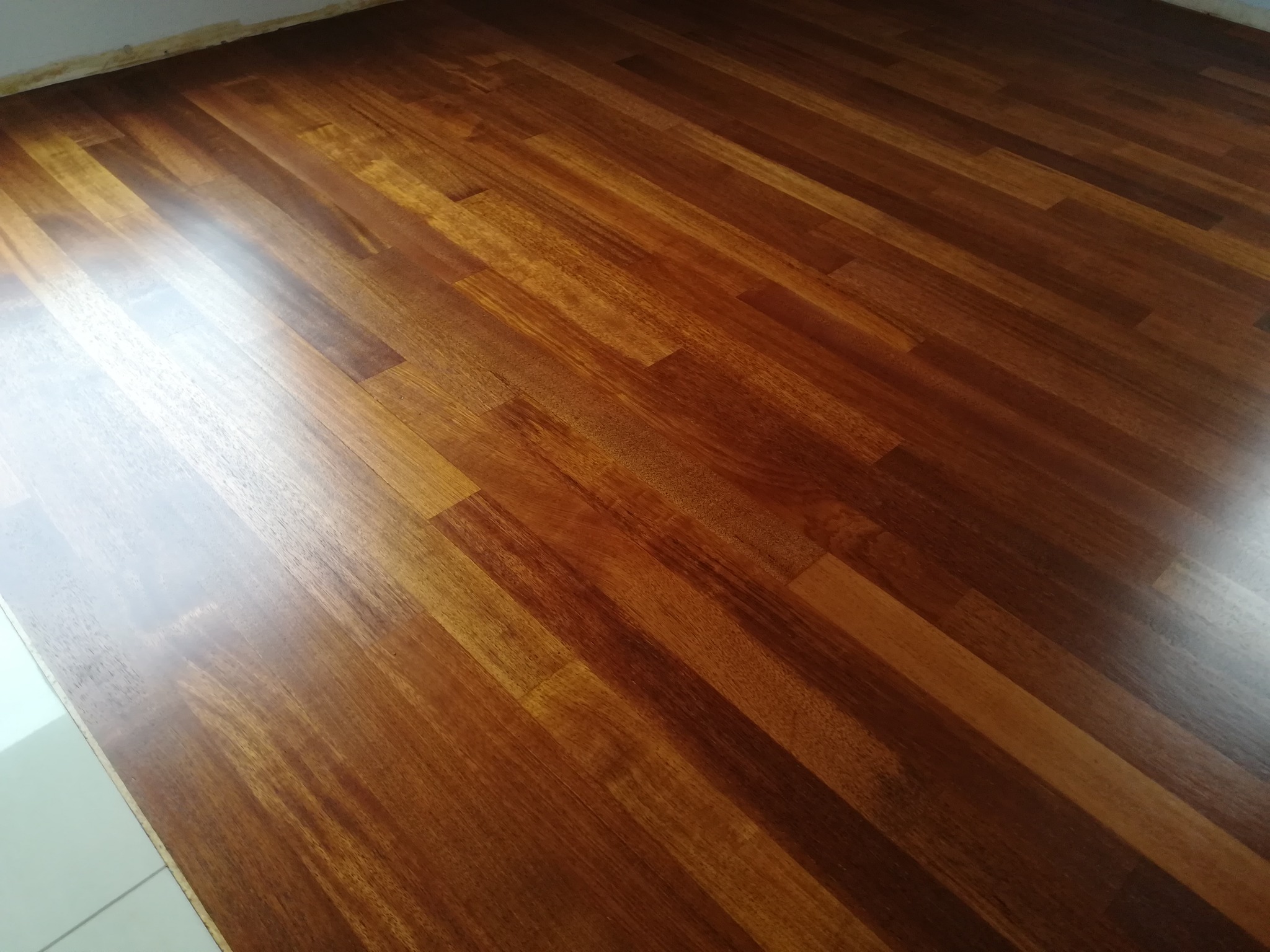 Błyszcząca, świeżo polakierowana podłoga z egzotycznego drewna ułożona w jodełkę, widoczne odbicia światła.