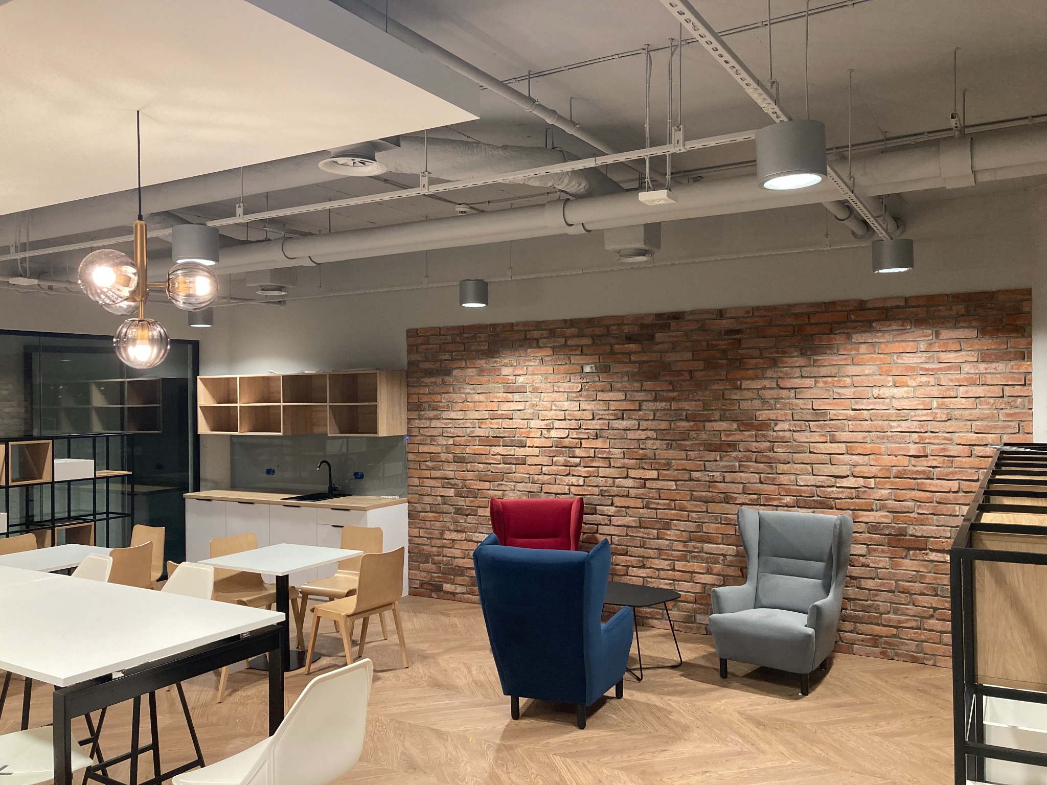 Nowoczesne biuro z odsłoniętymi instalacjami pod sufitem, designerskimi lampami i ceglaną ścianą.