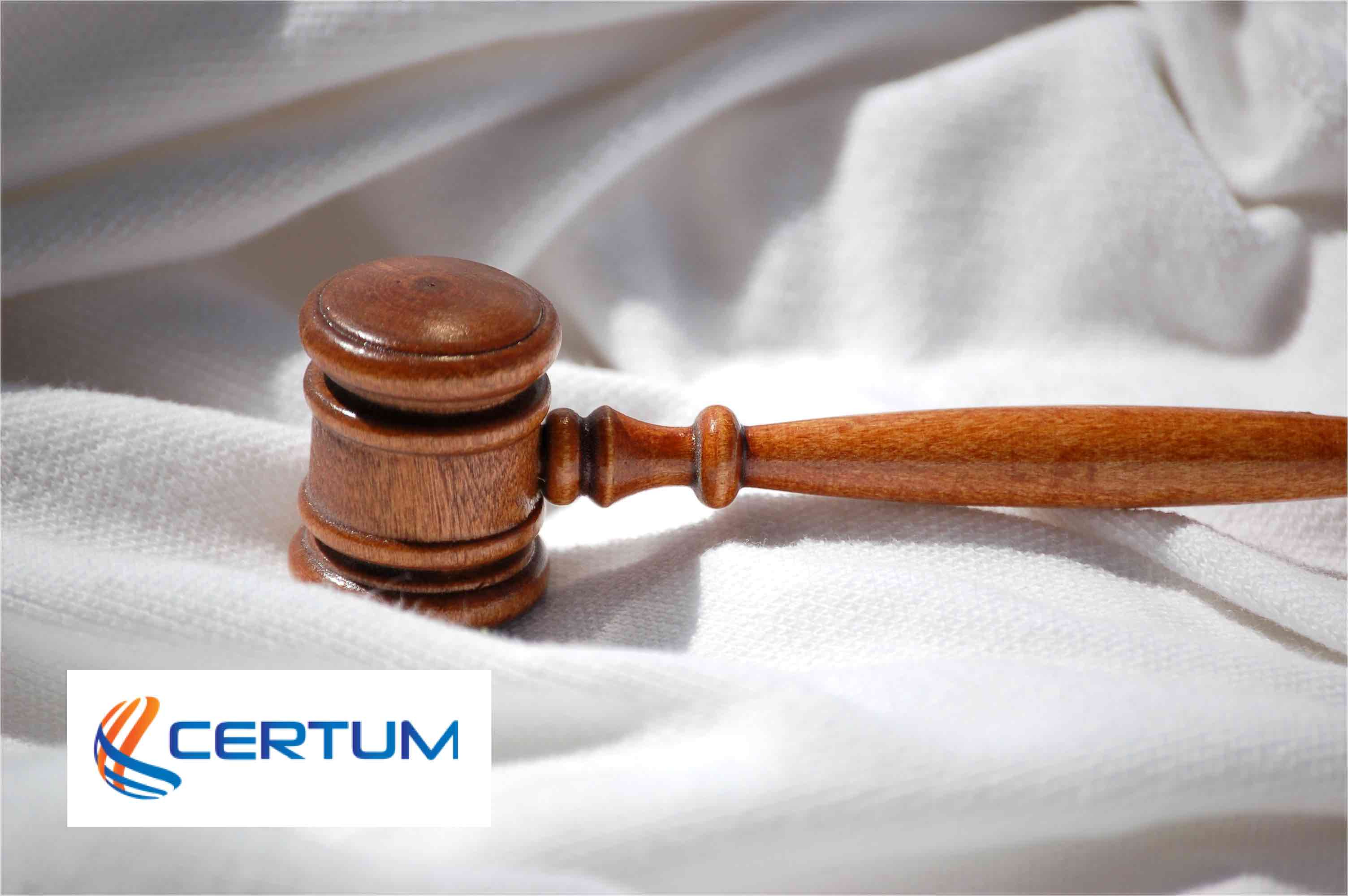 Drewniany młotek sędziowski na pogniecionej, białej tkaninie z logotypem firmy Certum w lewym dolnym rogu.