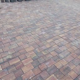 HYDRO-MAR SUSŁYK - Fragment nowej nawierzchni z kostki brukowej w odcieniach brązu i szarości, z widocznymi narzędziami brukarskimi i stosem kostek w tle.