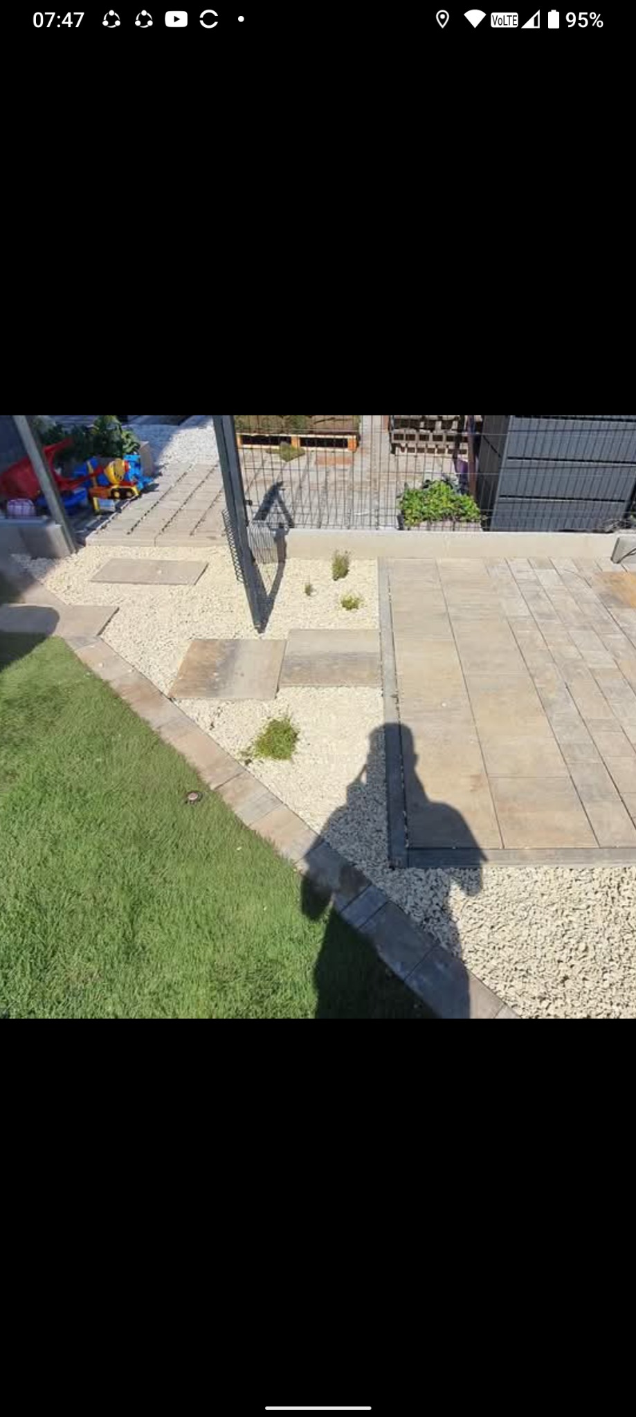 Ułożona kostka brukowa w Sompolno z jasnym żwirem i zielonym trawnikiem. Cień osoby na kostce. Estetyczne wykończenie ogrodu.