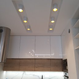 ARGIPS Arkadiusz Książek - Nowoczesna kuchnia z białymi szafkami, drewnianymi frontami i marmurowym backsplashiem. Sufit z wbudowanymi, okrągłymi lampami punktowymi. Minimalistyczny design.