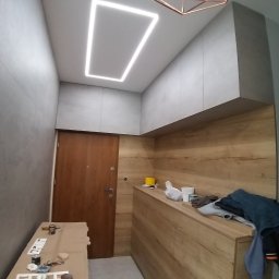 ARGIPS Arkadiusz Książek - Nowoczesne wykończenie przedpokoju: drewnopodobne panele ścienne, szare szafki pod sufitem i minimalistyczna lampa sufitowa z kwadratowym oświetleniem LED.