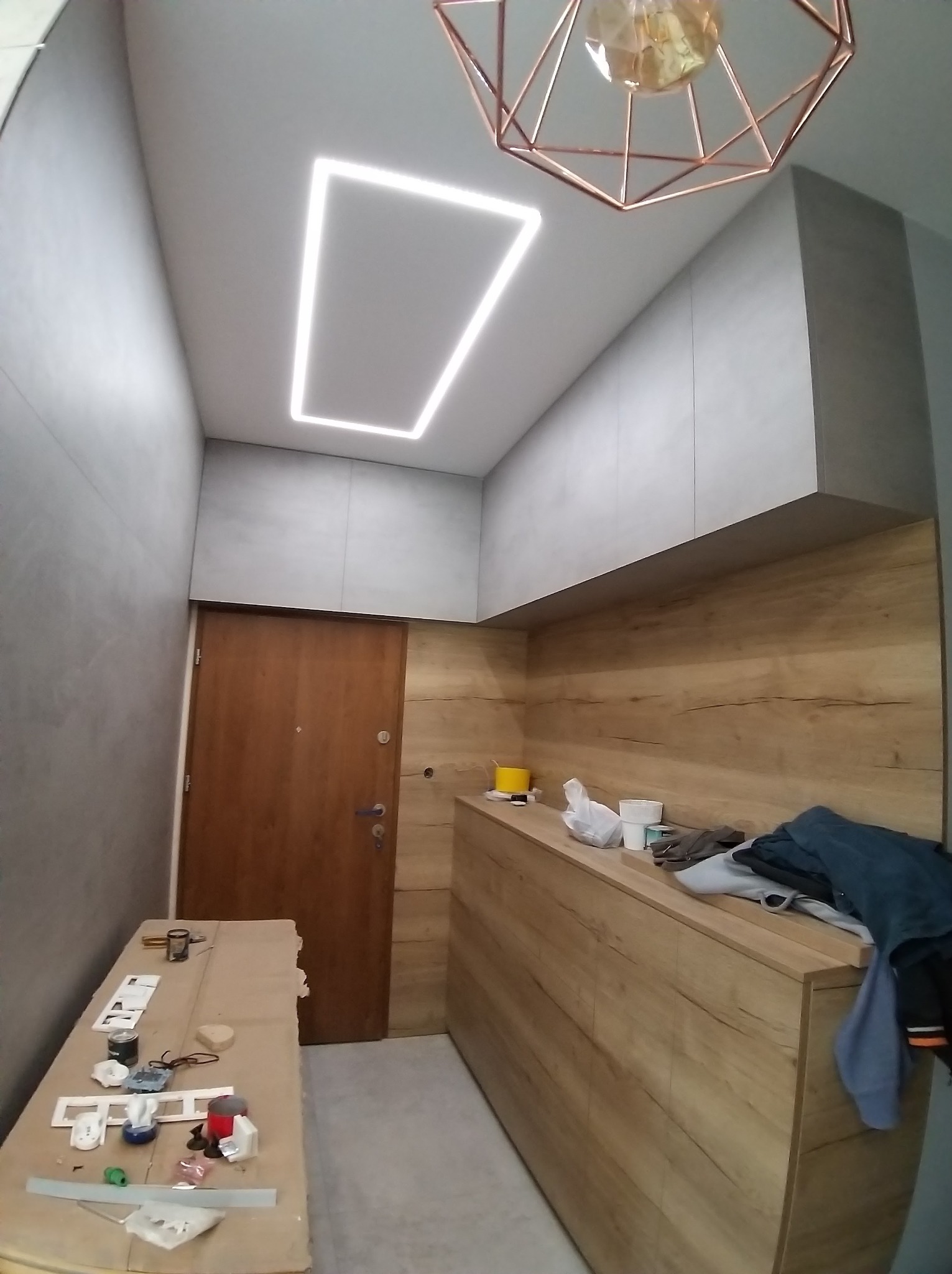 Nowoczesne wykończenie przedpokoju: drewnopodobne panele ścienne, szare szafki pod sufitem i minimalistyczna lampa sufitowa z kwadratowym oświetleniem LED.
