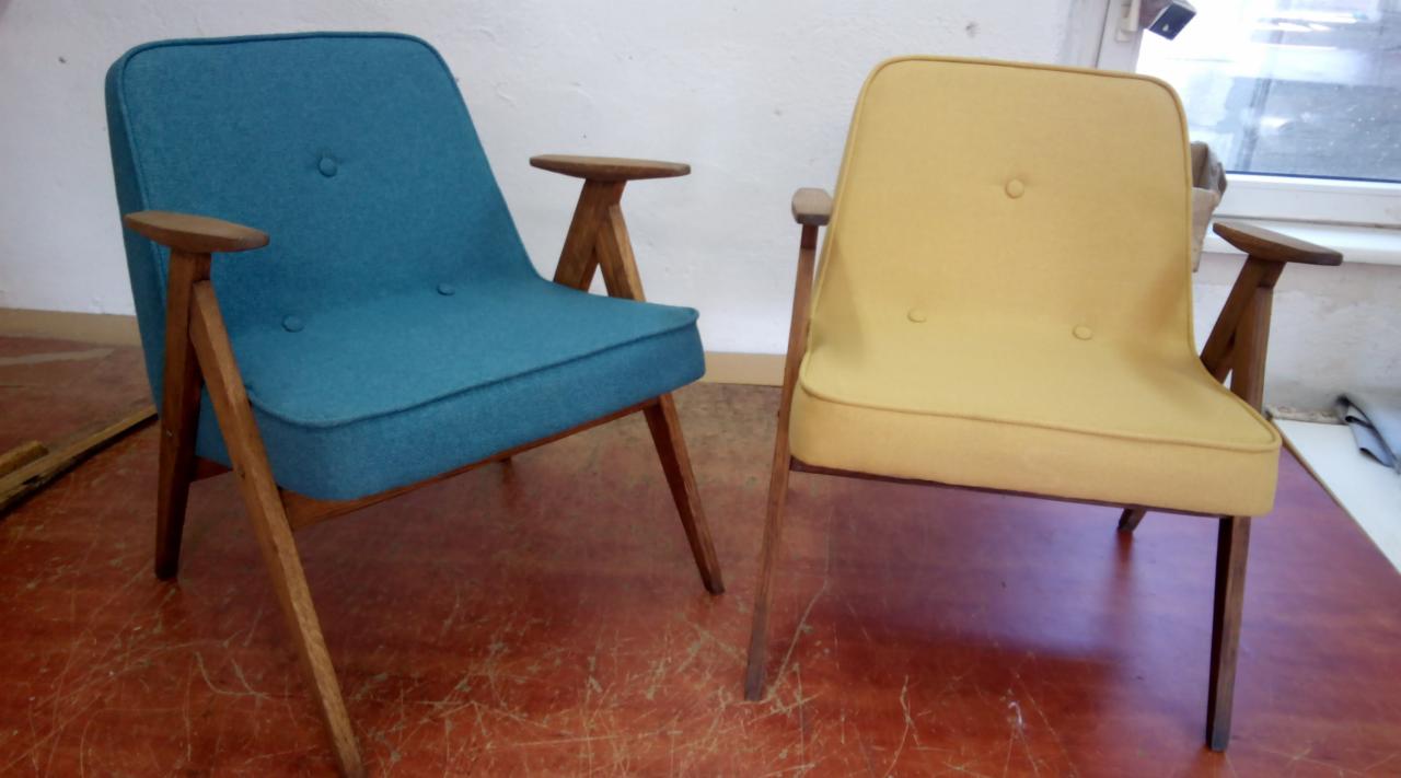Dwa odnowione fotele w stylu retro: turkusowy i żółty, z drewnianymi podłokietnikami w kształcie litery T, stojące na czerwonej podłodze z widocznymi śladami użytkowania.