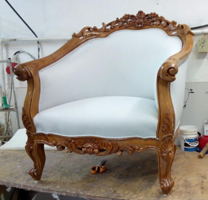 Odrestaurowany fotel w stylu Ludwika, z jasną tapicerką i ozdobną, rzeźbioną drewnianą ramą, widoczne nożyczki tapicerskie na blacie roboczym.