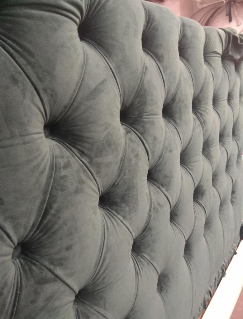 Tapicerowana, ciemnoszara wezgłowie łóżka w stylu chesterfield z głębokimi pikowaniami i guzikami, widok z boku.