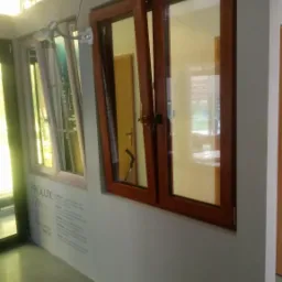 Ekspozycja dwóch okien: jedno drewniane, otwarte, drugie z ramą w jasnym kolorze, z widocznymi napisami reklamowymi na ścianie obok.