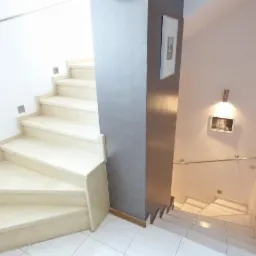 Wnętrze w Katowicach z marmurowymi schodami, gdzie ściany są w odcieniach bieli i szarości, a na ścianie wisi oświetlony obrazek.