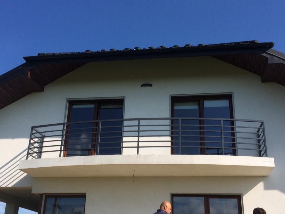 Balkon z prostą, metalową konstrukcją zabezpieczającą w Tarnowie, widok z dołu, jasne niebo w tle.