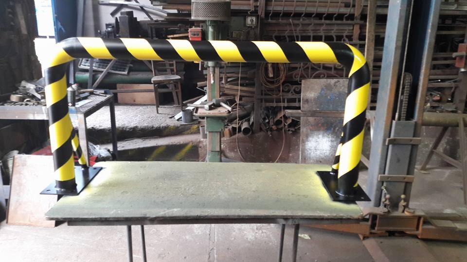 Metalowa bariera ochronna z czarno-żółtymi pasami, zamontowana na metalowej platformie w warsztacie.