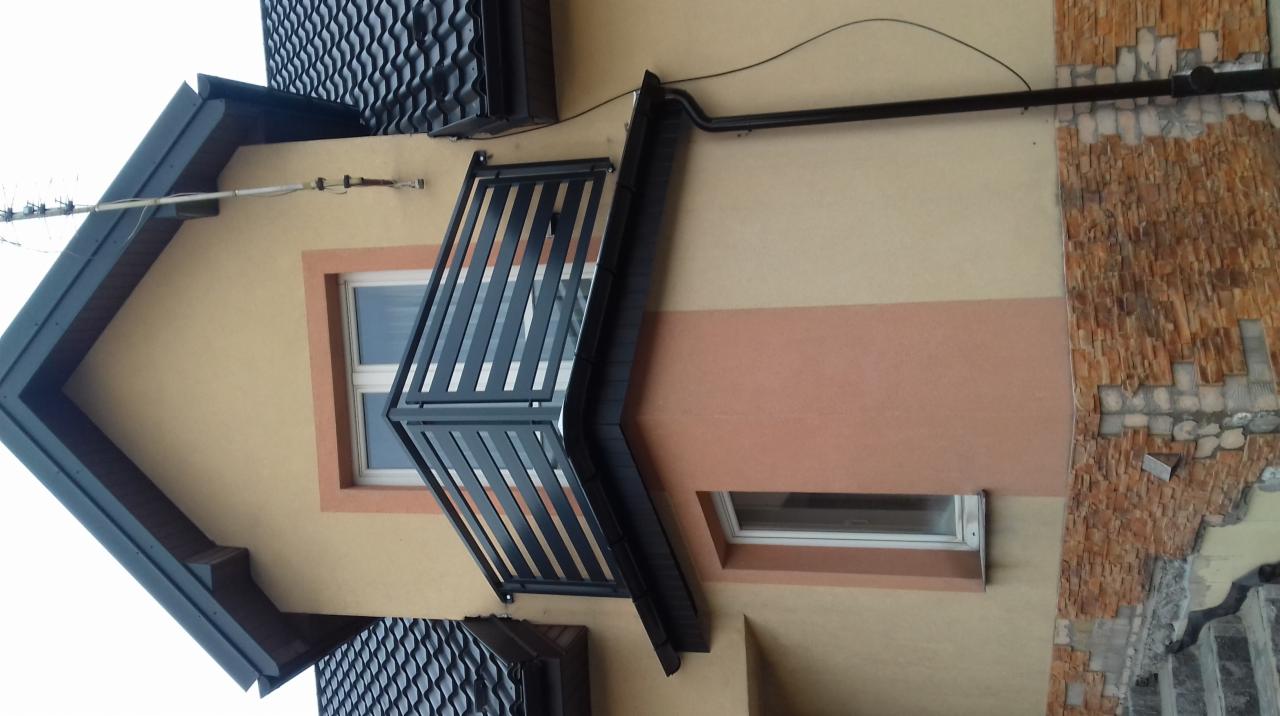 Czarny balkon z pionowymi szczebelkami, zamontowany na elewacji domu z oknami i dekoracyjną okładziną z kamienia.