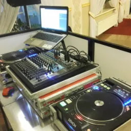 Stanowisko DJ-a z dwoma gramofonami Denon DN-S3700, mikserem dźwięku i laptopem ASUS na statywie, otoczone dekoracjami sali weselnej.