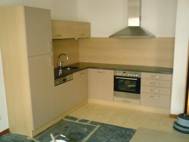 Kątowe ujęcie beżowej kuchni z czarnym blatem, osłoniętą folią podłogą i widocznym okapem nad płytą.