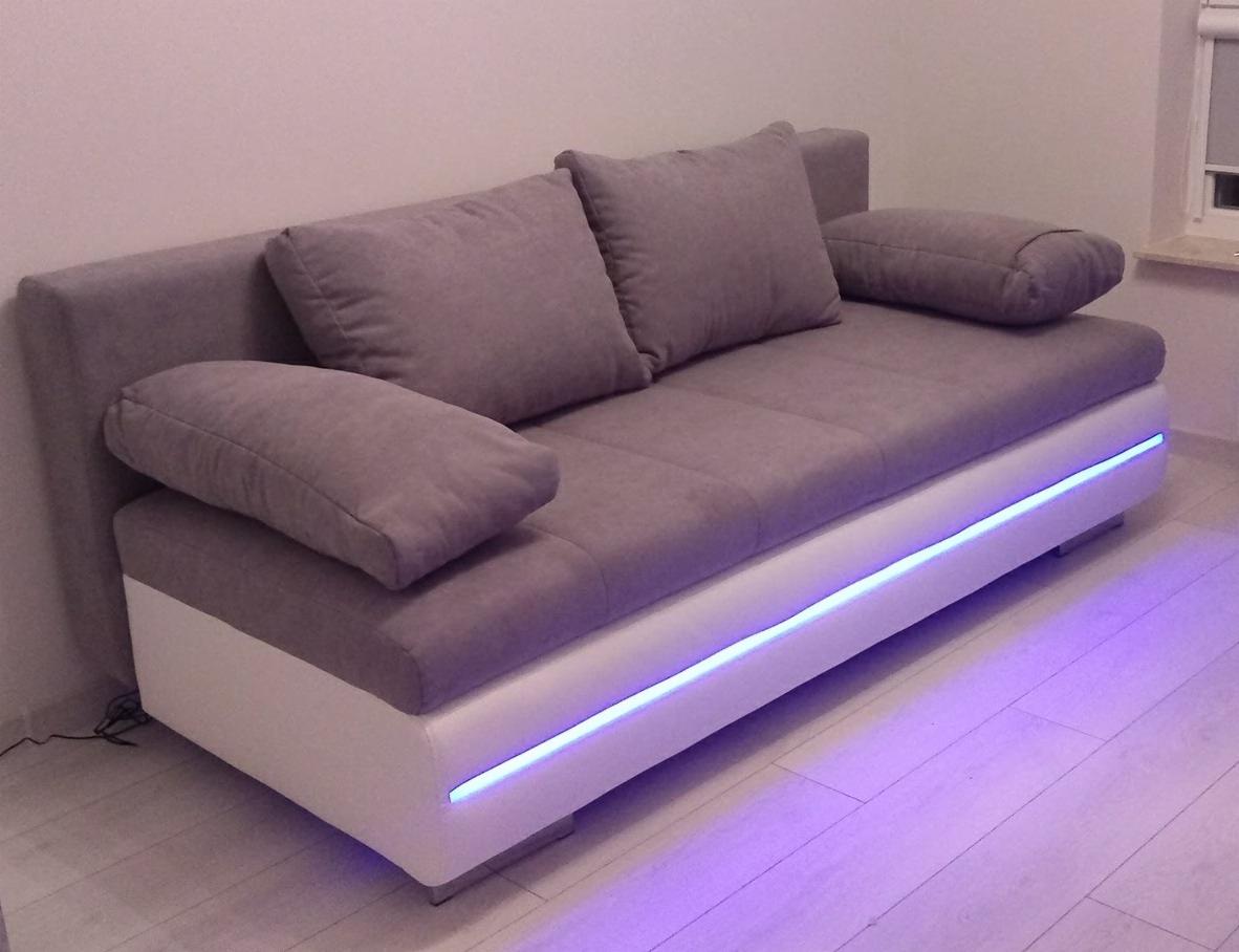 Nowoczesna szara sofa z białym wykończeniem i subtelnym niebieskim podświetleniem LED, ustawiona w minimalistycznym wnętrzu.