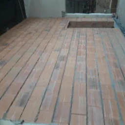 Wnętrze w trakcie budowy, widoczny fragment podłogi z ułożonymi bloczkami ceramicznymi, przygotowanymi do dalszych prac wykończeniowych.